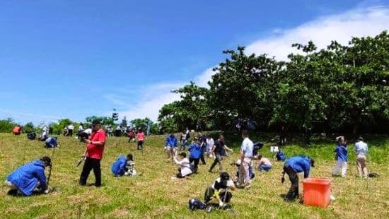 高雄都會公園二期園區植樹活動現場，參與者們在藍天白雲下積極進行植樹，種下200棵原生喬木，展現出熱情與活力。